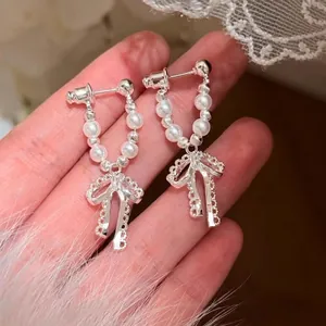 Primo piano di orecchini a fiocco argentati con eleganti perle finte in mano.