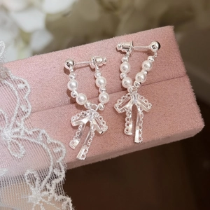 Dettaglio di eleganti orecchini a fiocco in argento con perle sintetiche su rosa