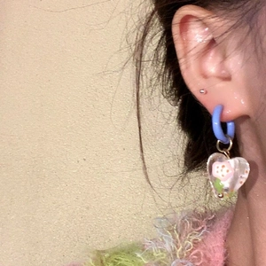 Nahaufnahme eines hellblauen Creolen-Ohrrings mit klarem Herzblumen-Anhänger am Ohr
