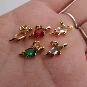 Macro shot of five gold-plated turtle charms with colorful cubic zirconia in hand palm