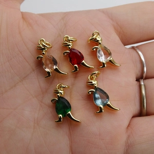 Five small dinosaur charms with colorful zircon gemstones displayed on a person's palm