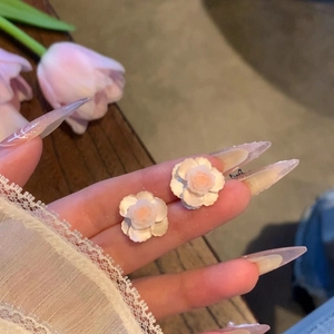 Macro detail of elegant white camellia flower stud earrings held on a fingertip