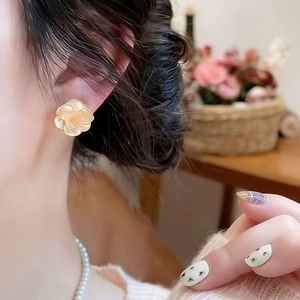 Detailed view of elegant cream-colored camellia flower stud earrings worn on a female ear