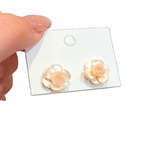 Elegant cream camellia flower stud earrings on white display card.