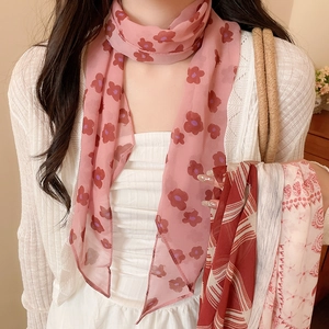 Close-up of a pink floral mesh scarf styled with a white cardigan and a straw bag.