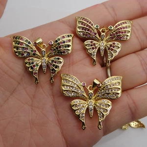 Three gold butterfly pendants with colorful zircon inlay held in hand for size context