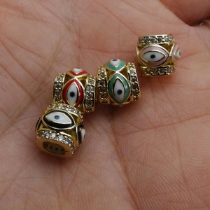 Handheld view of four 14K gold plated evil eye beads with enamel and crystals