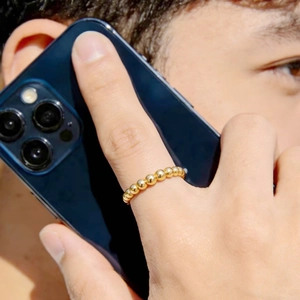 Close-up view of a 2mm gold bead titanium steel ring worn on a finger while holding a smartphone