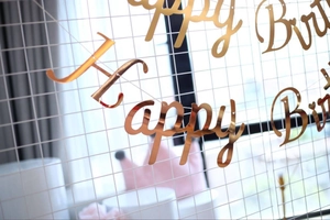 Close-up of rose gold cursive Happy Birthday banner hanging on a white grid backdrop