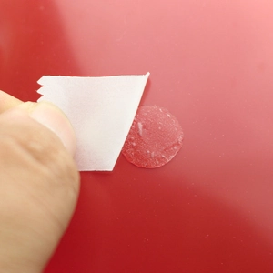 Vue macro d'un patch adhésif rond rouge avec papier protecteur retiré à la main