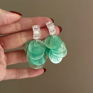 Dettaglio degli orecchini con zirconi e dischi di conchiglia verde menta nella mano