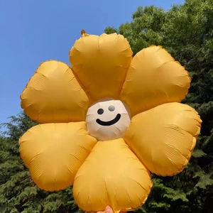 Large yellow daisy flower foil balloon with white center and black smiley face outdoors