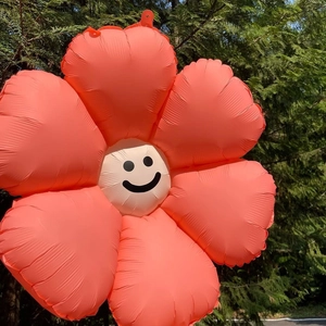 Close-up of coral orange daisy flower foil balloon with a smiling face in natural outdoor setting