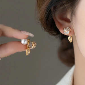 Detailed view of camellia stud earrings with pearl and gold leaf charms on model.
