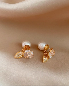 Detailed view of camellia flower pearl earrings with zircon leaf charms on silk background.