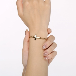 Close-up detail of a minimalist gold stainless steel cross bracelet worn on a wrist.