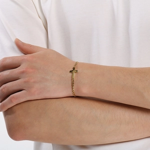 Close-up of a gold stainless steel cross bracelet worn on a wrist against white shirt
