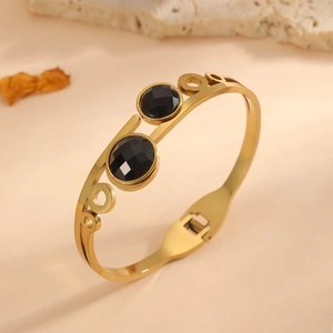 Detailed macro shot of gold titanium steel bangle with two faceted black stones.