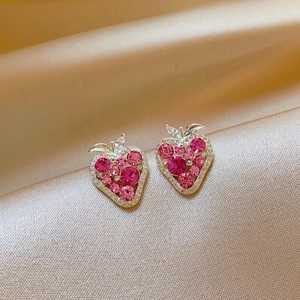 Close-up detail of strawberry-shaped earrings with sparkling pink zircon stones on silk.