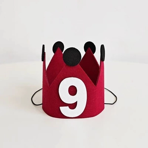 Detail of red felt birthday crown with number 9 and black pom-poms on white background