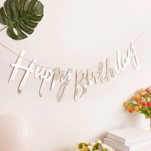Silver mirror Happy Birthday banner hanging on wall with flowers and party decorations