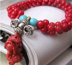 Macro view of red beaded bracelet with silver vajra charm and blue spacer beads on paper