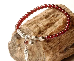 Pulsera retro de cuentas rojas con dijes de maní y campana de plata sobre fondo de piedra