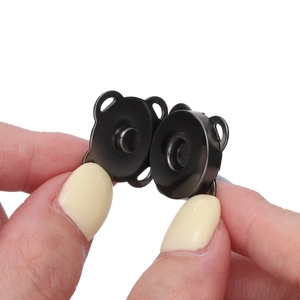 Macro view of hand holding dark metallic magnetic snap buttons for bags and clothing