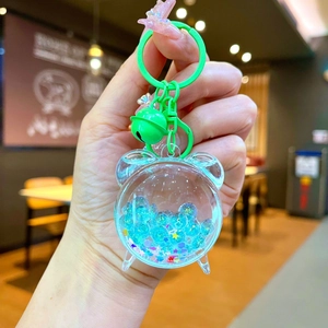 Close-up of green bear-shaped liquid sand keychain with blue glitter and metal bell
