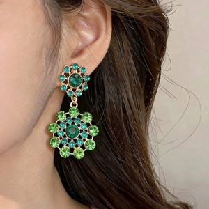 Close-up of vintage gold flower earrings with sparkling green crystals and palace style.