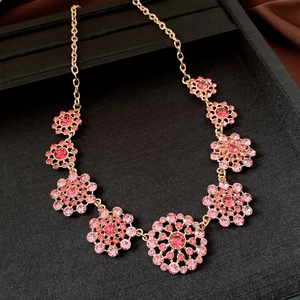 Detail view of vintage hollowed round necklace with pink crystals on black display box.