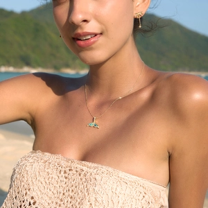 Detailaufnahme einer goldenen Walflossen-Halskette mit Abalone-Muschel am Strand