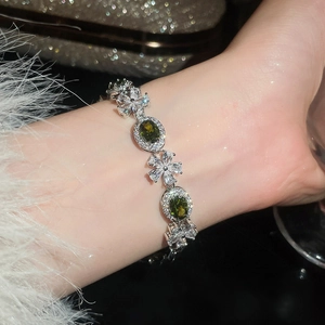 Detailaufnahme eines luxuriösen Silberarmbands mit grünen Zirkonia-Ovalen und Blumenanhängern