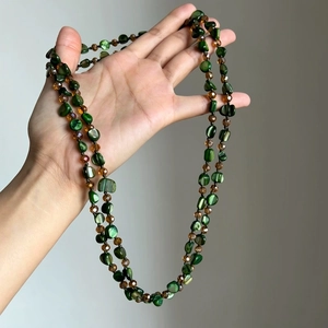 Close-up of bohemian long necklace with green shell beads and amber crystals held by hand