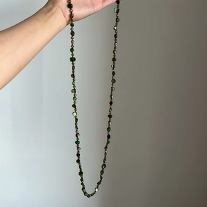 Hand-held view of a long bohemian style necklace with green shell beads and brown accents