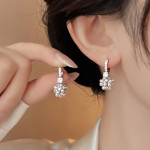 Dettaglio macro di orecchini a pendente con zirconi e perle, finitura argento elegante