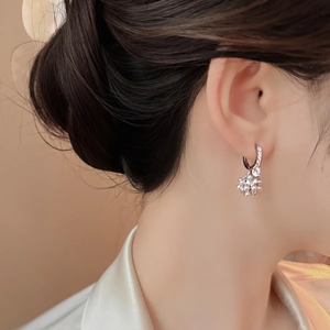 Dettaglio di un elegante orecchino a cerchio con fiori di zirconi e perle indossato
