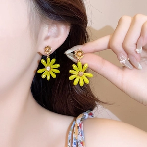 Detailed view of vibrant yellow daisy flower drop earrings worn by a female model