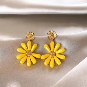 Detail view of stylish yellow daisy drop earrings resting on soft champagne satin fabric