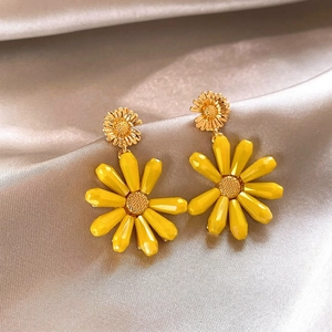 Detail macro view of vibrant yellow daisy drop earrings on a luxurious silk background