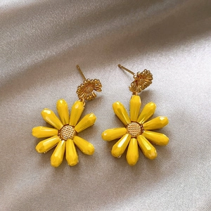 Detail view of vibrant yellow daisy earrings with gold accents on satin.