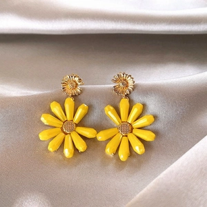 Detailed close-up showing bright yellow daisy flower drop earrings on silky fabric