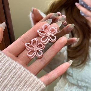 Detailed macro view of sweet pink hollow flower-shaped stud earrings held by a hand