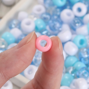 Macro detail of a colorful acrylic large hole bead held between fingers for DIY crafts