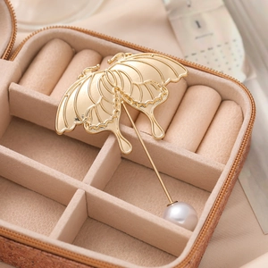 Detailed close-up of a gold butterfly brooch with a lustrous white pearl in a velvet box