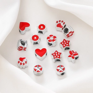 Macro shot of silver metal beads with red enamel star, heart, and claw shapes