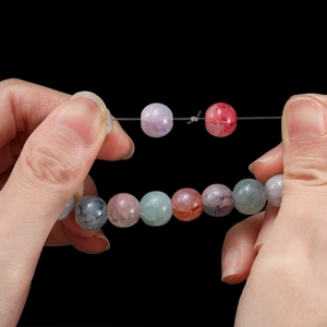 Nahaufnahme bunter Kristallperlen mit elastischem Faden beim Dehnen und Knoten