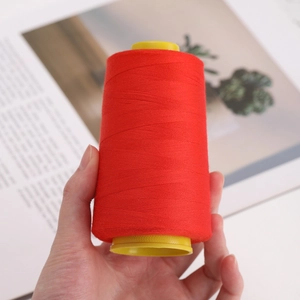 Single roll of red polyester 402 sewing thread on yellow spool held in hand