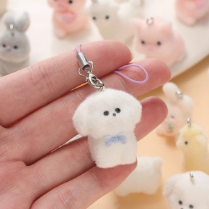Cute white Bichon dog plush keychain with blue bow and purple strap held in hand