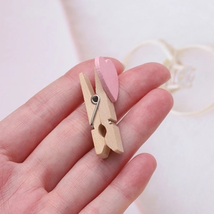 Mini molletta in legno per foto con cuore rosa tenuta in mano per mostrare le dimensioni